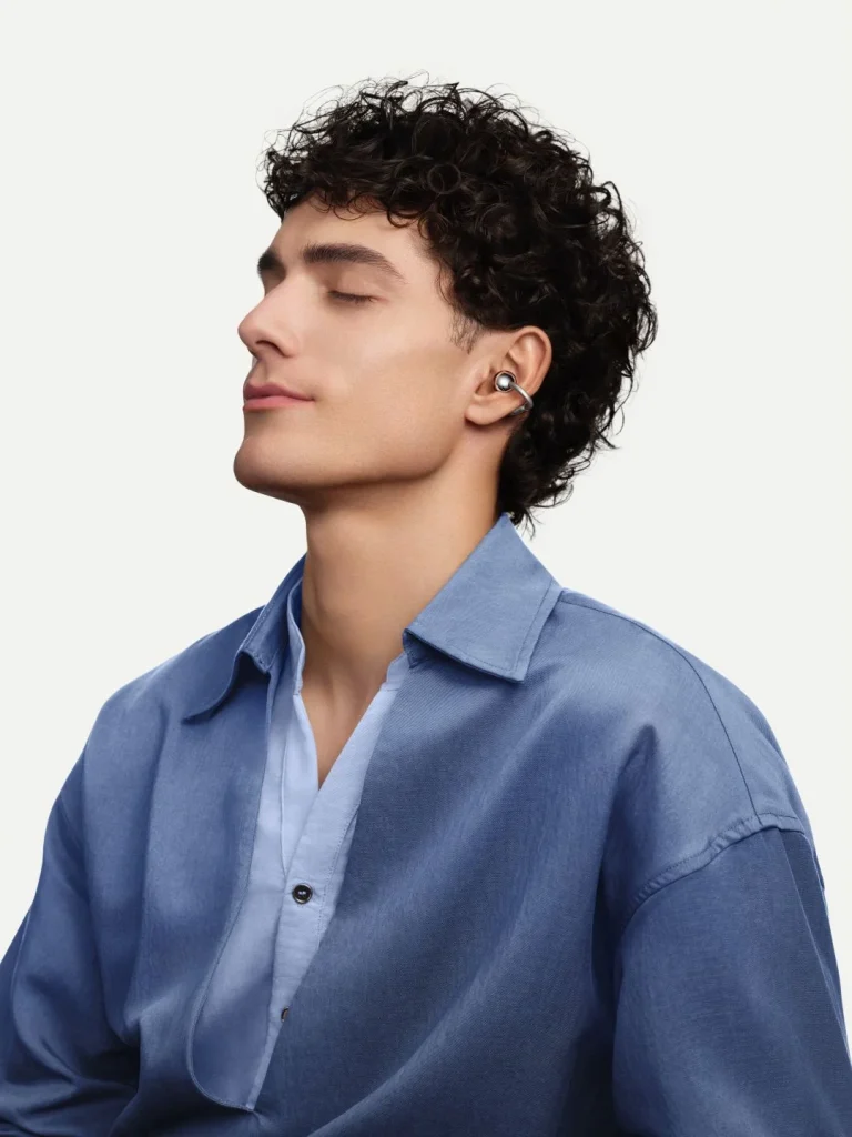Homem com cabelo encaracolado a usar auriculares prateados abertos.