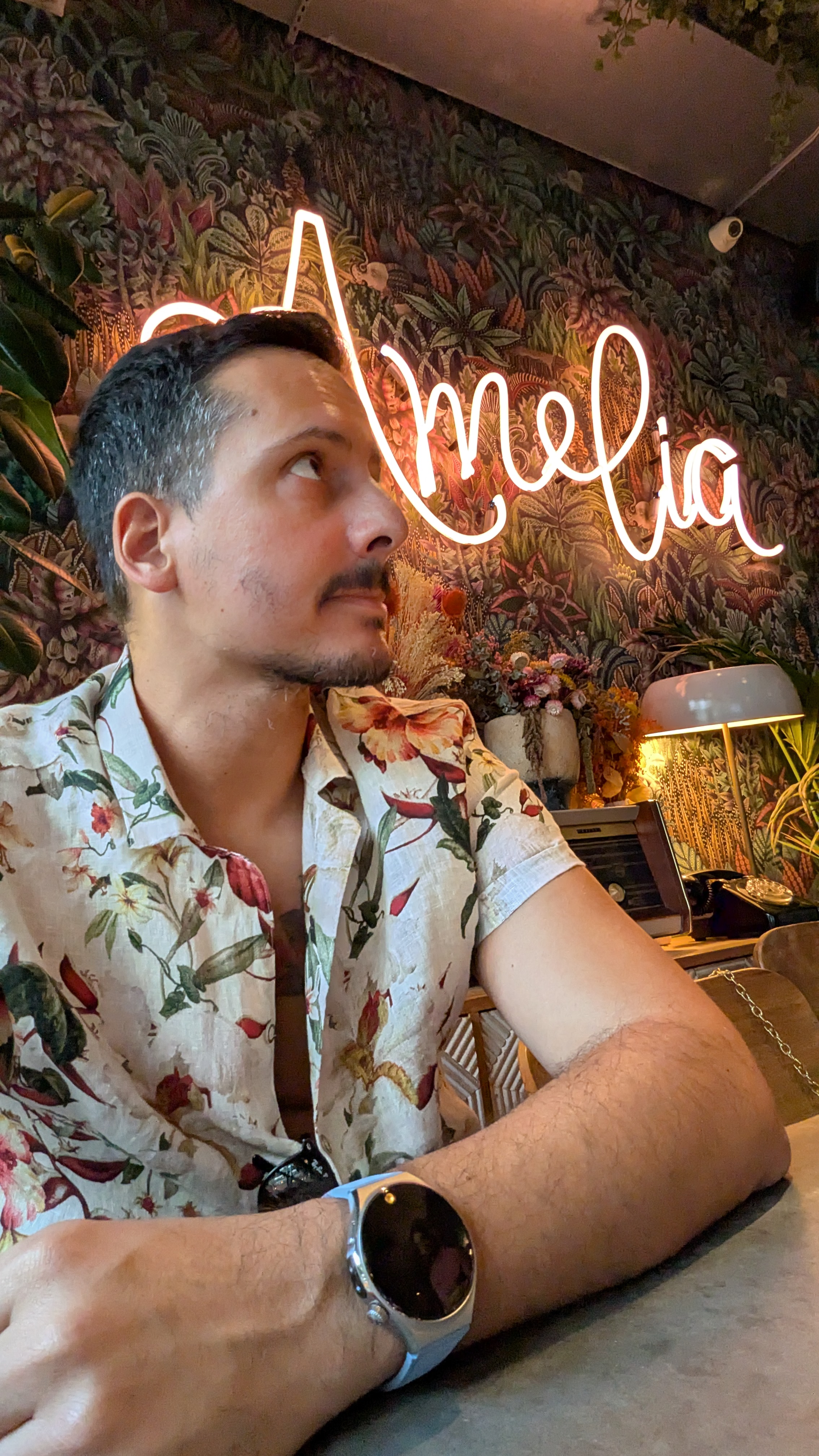 Homem com camisa floral sentado num espaço com luz néon a usar o smartwatch Huawei Watch 6 no pulso