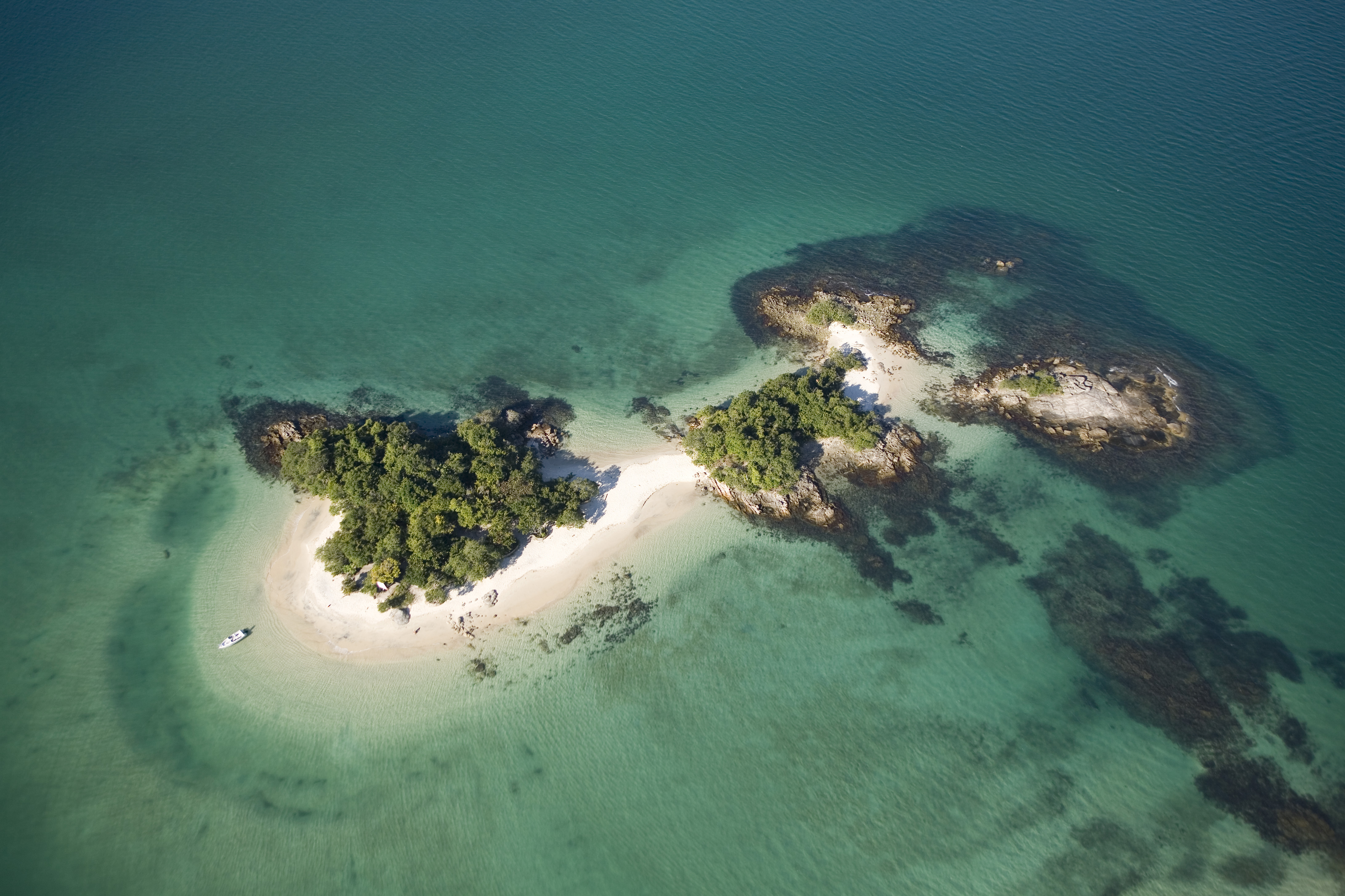 Vista aérea de uma pequena ilha tropical com árvores verdes e praias de areia branca banhadas por águas turquesa numa rota de cruzeiro na América do Sul.