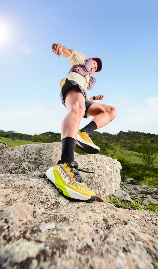 Corredor de trail a saltar entre rochas com sapatilhas amarelas.