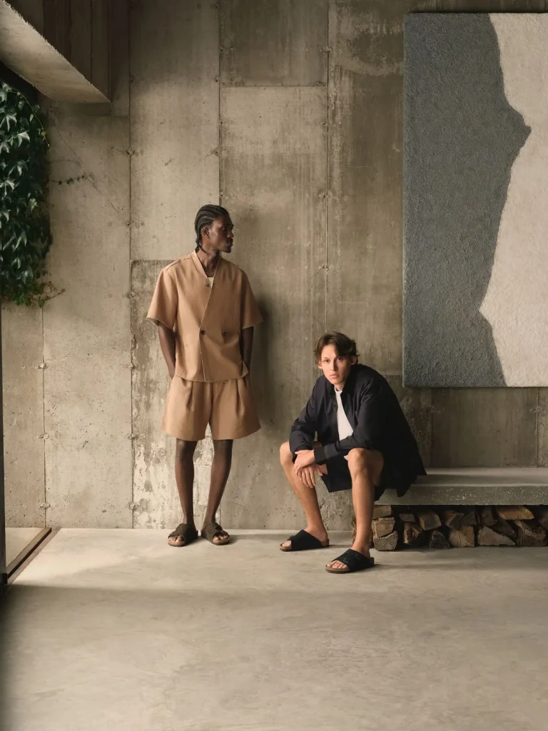 Dois homens posam com roupa casual num interior de betão.