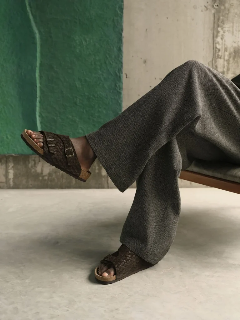 Pessoa sentada com calças largas e sandálias Birkenstock castanhas.