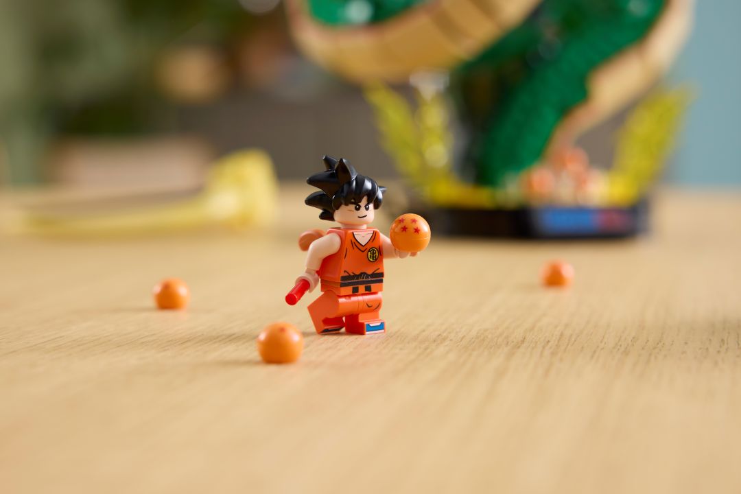 Minifigura lego songoku com fato laranja a segurar uma esfera do dragão e um bastão vermelho sobre uma mesa de madeira