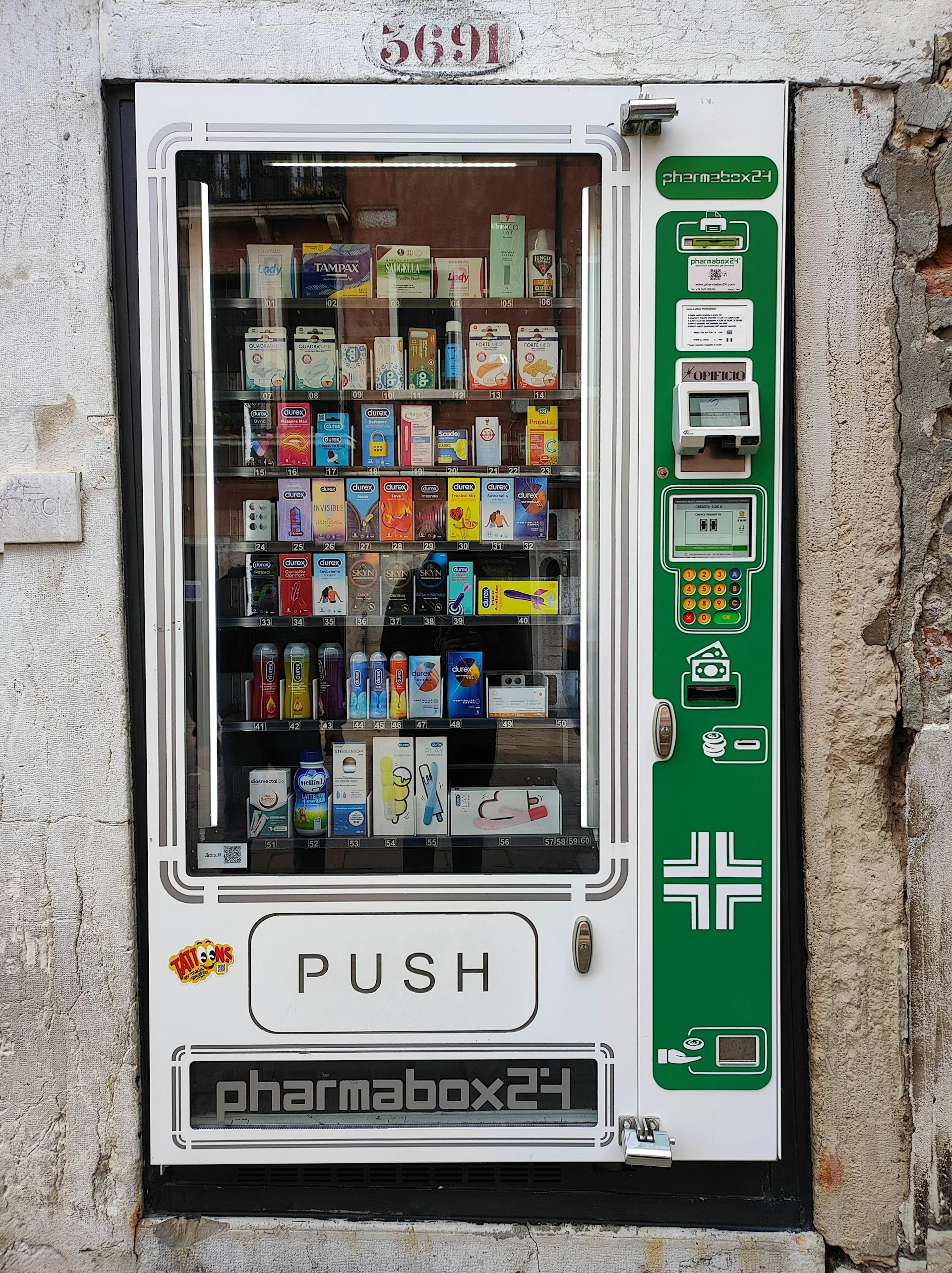 Máquina de venda automática pharmabox24 embutida numa parede de pedra com várias caixas de preservativo ultrafino e produtos de farmácia.