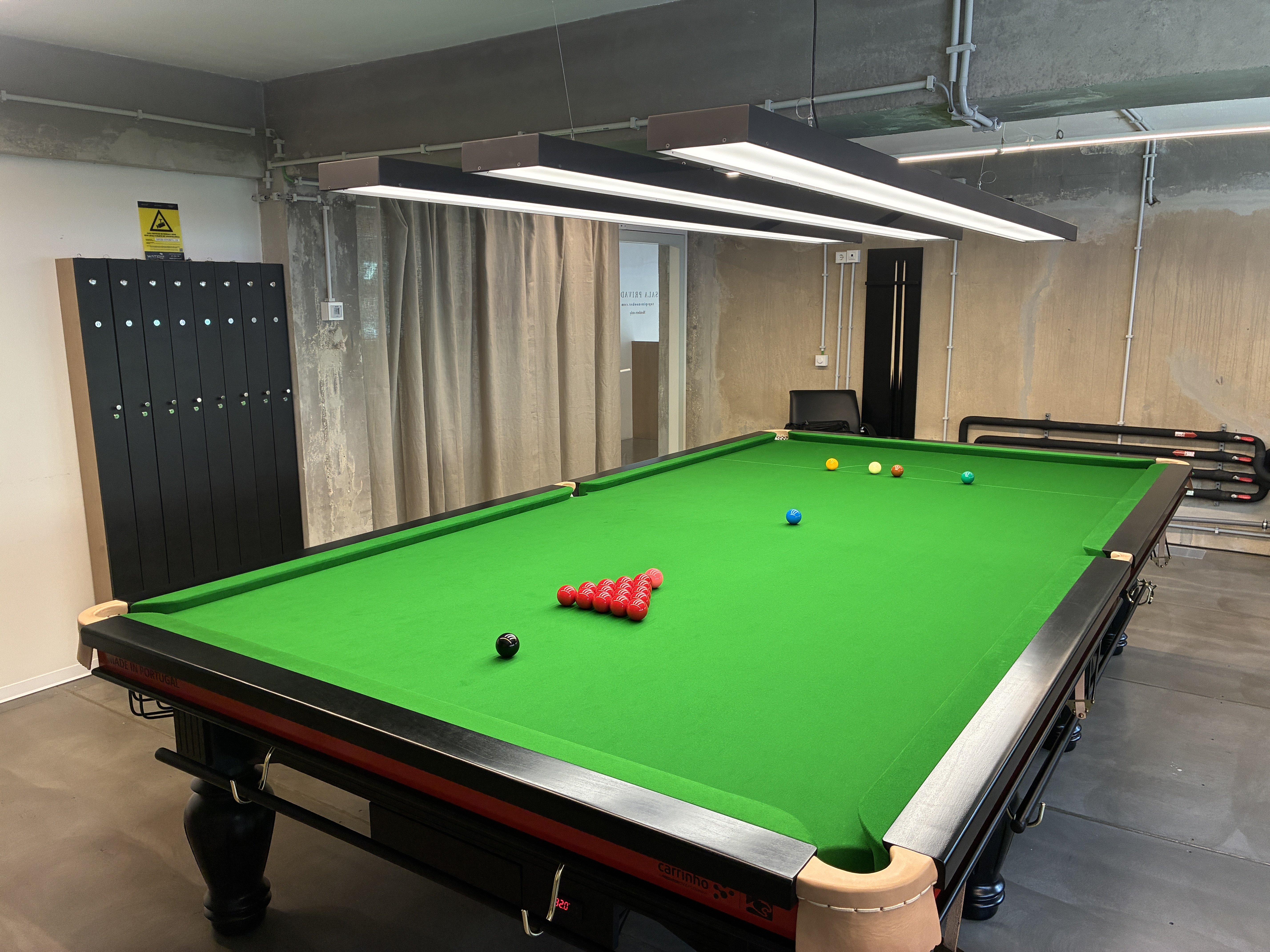 Mesa de snooker profissional com pano verde e bolas posicionadas sob iluminação suspensa num clube de snooker em Lisboa.