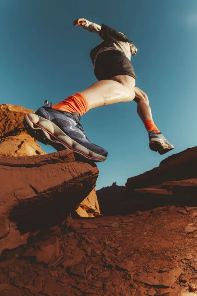 Pessoa a saltar sobre rochas vermelhas com ténis de trail.