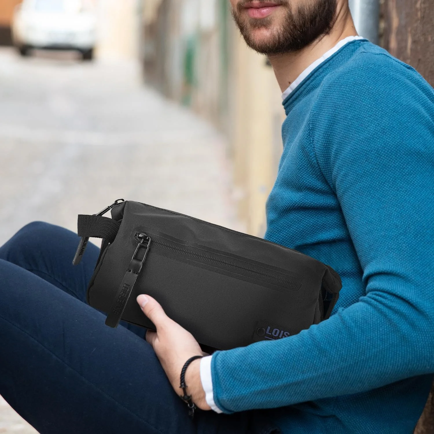 Homem com camisola azul a segurar no colo um necessaire de viagem para homem preto da marca Lois.