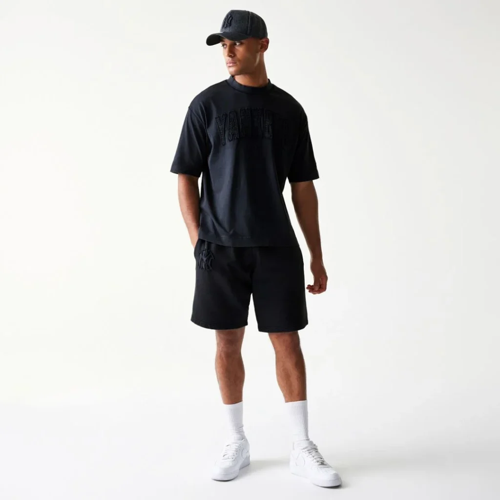 Homem com conjunto preto Yankees e boné.