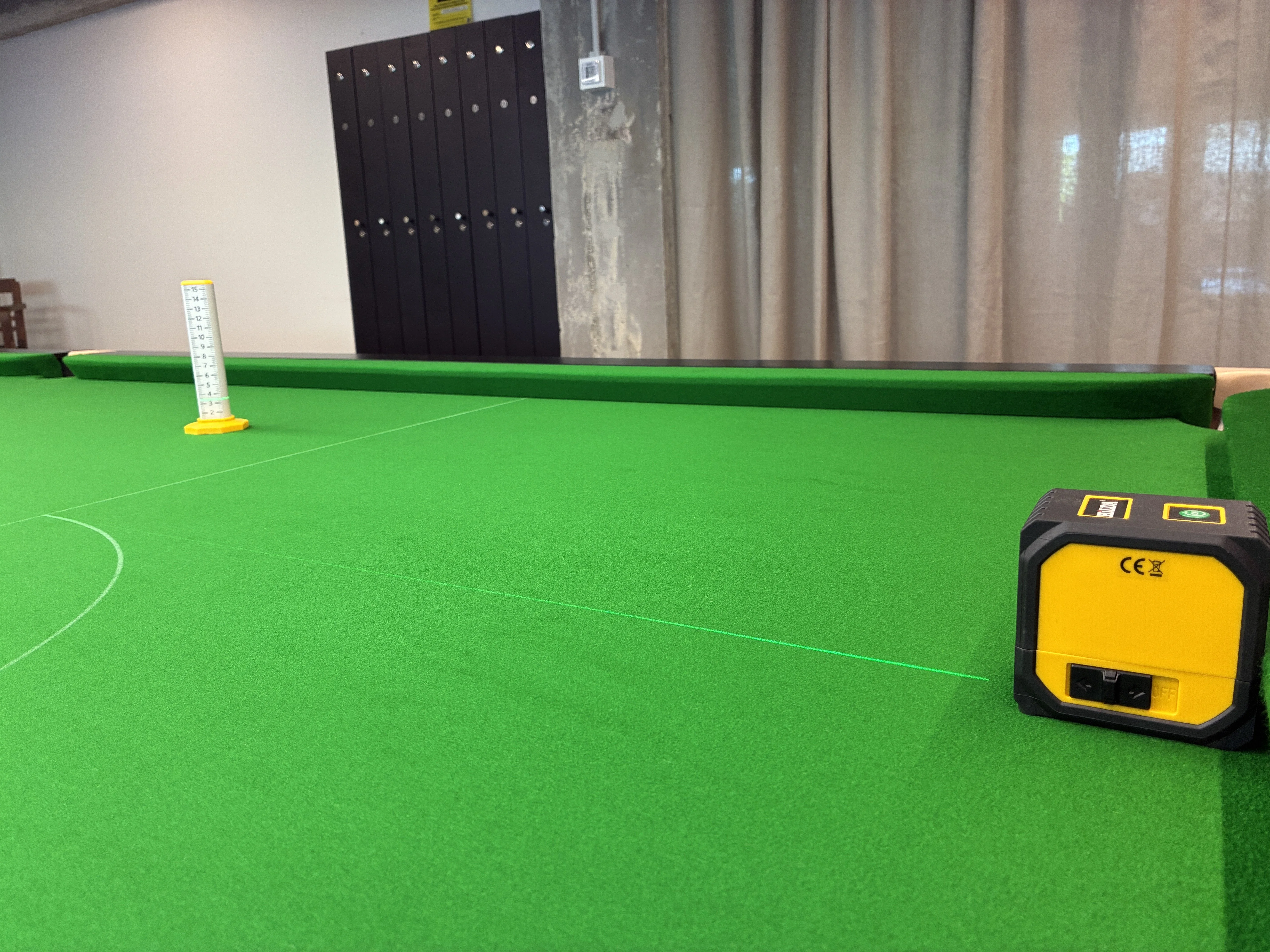Aparelho de nivelamento a laser projetando uma linha verde no pano de uma mesa de snooker no Top Spin Snooker, com um alvo de medição branco