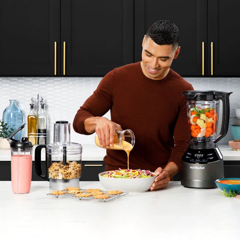 Homem prepara salada com liquidificador em cozinha moderna.