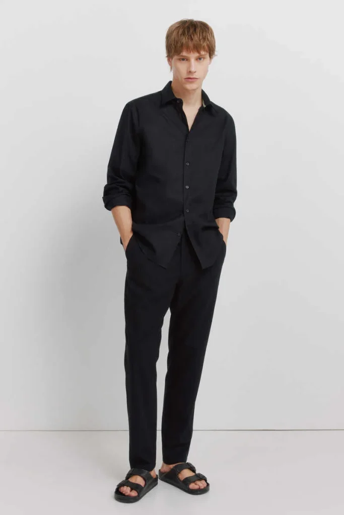 Jovem com camisa preta, calças pretas e sandálias.