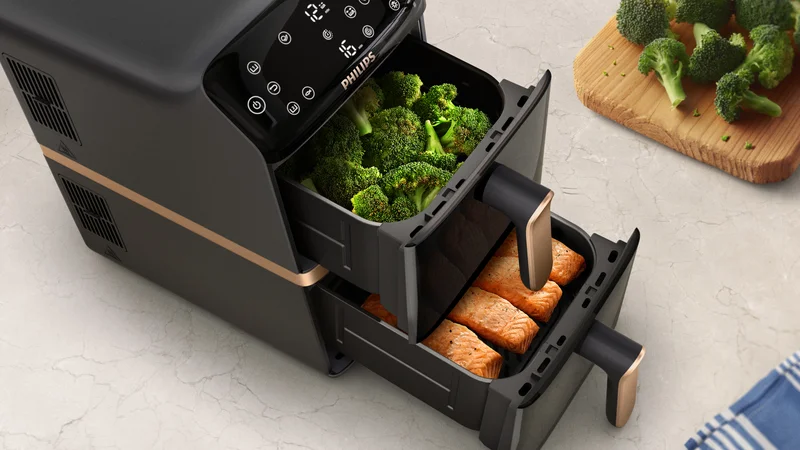 Airfryer Philips com duas gavetas abertas com brócolos e salmão.
