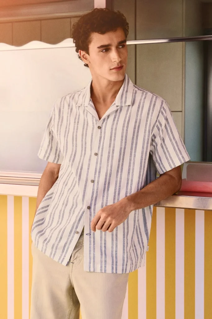 Homem de camisa às riscas azuis e brancas em ambiente de verão.