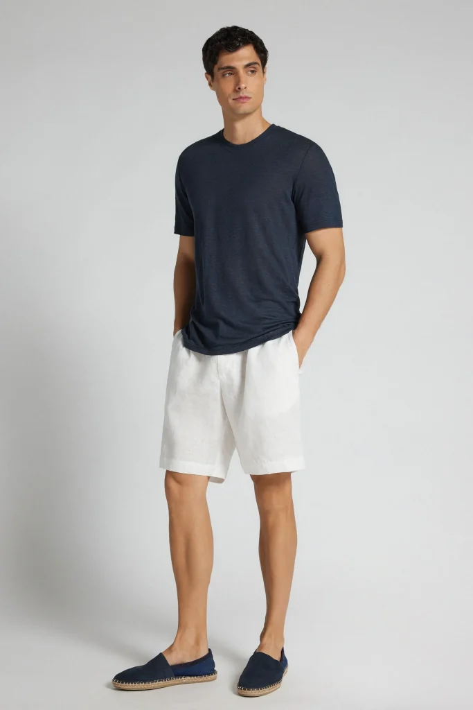 Homem com t-shirt azul marinho e calções brancos de linho.