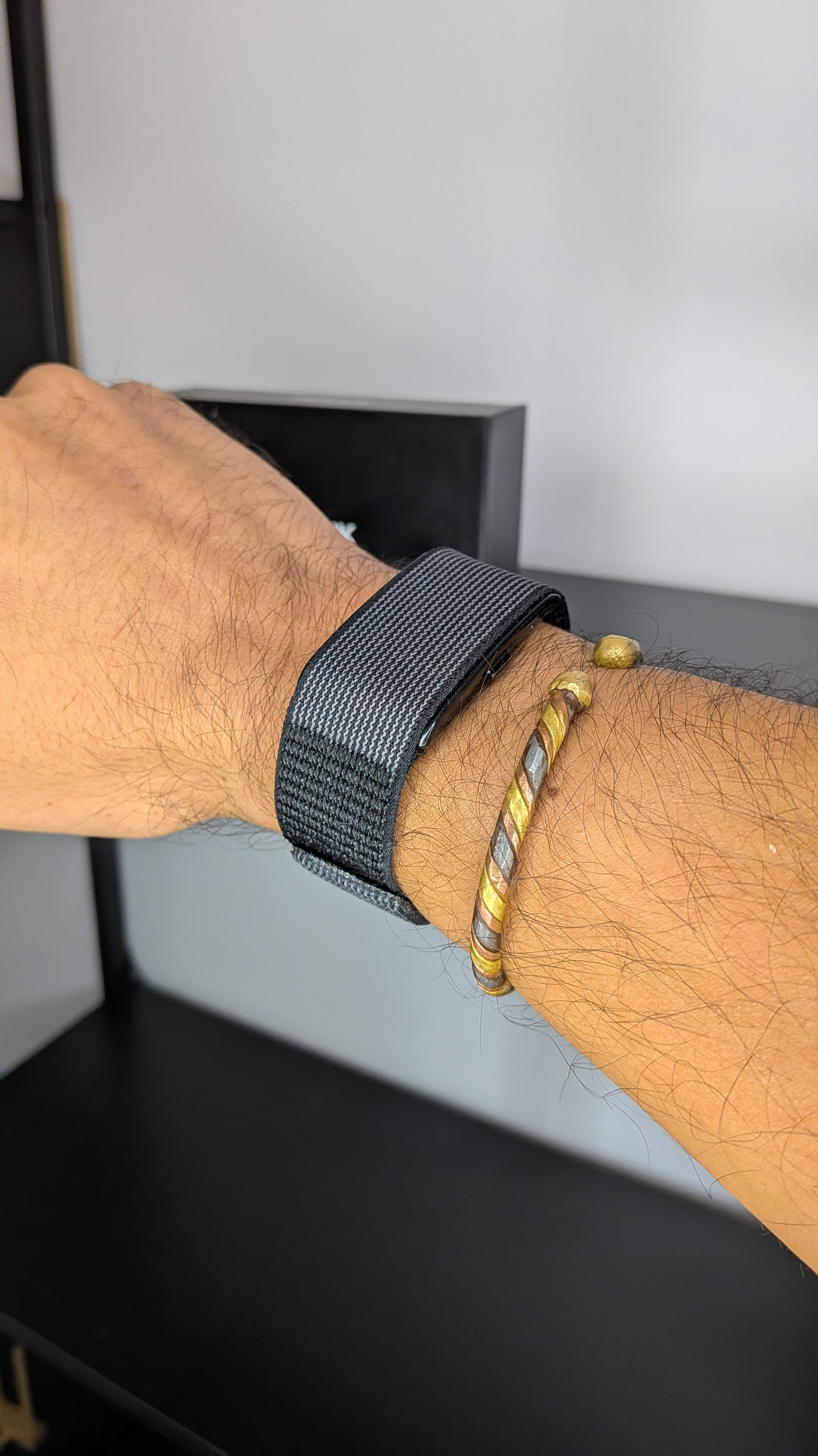 Pulso masculino a usar a pulseira desportiva DuckDik Sense preta com bracelete de tecido texturizado ao lado de uma pulseira metálica
