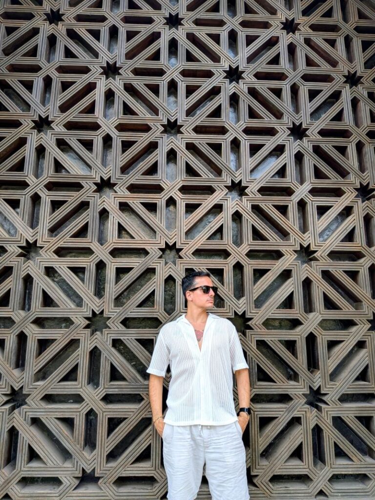 Homem em frente a parede geométrica ornamentada.
