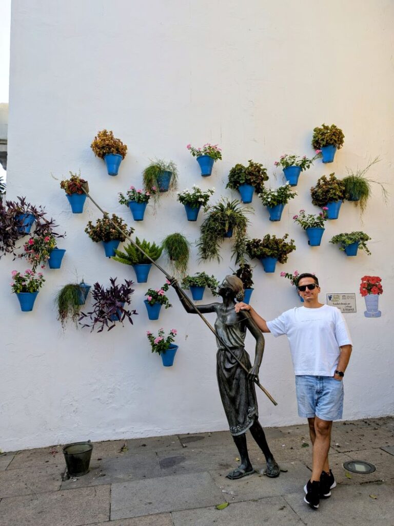 Homem e estátua em parede com vasos de flores.
