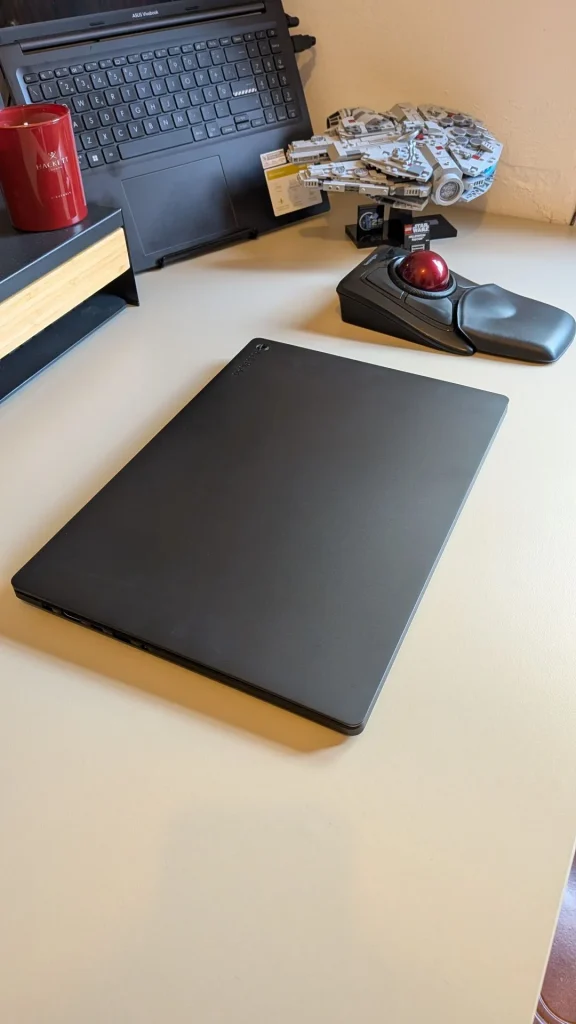 Mesa com portátil fechado, rato trackball e decoração.