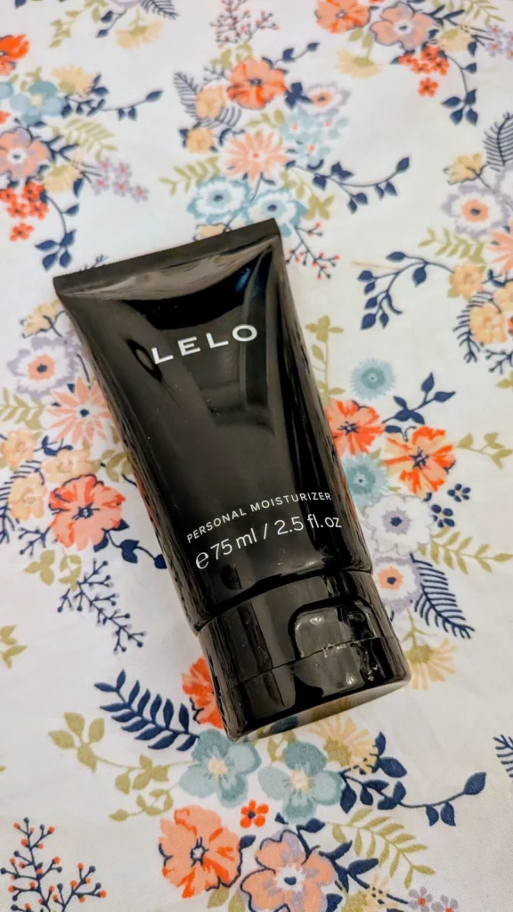 Tubo de hidratante pessoal LELO preto sobre fundo floral.