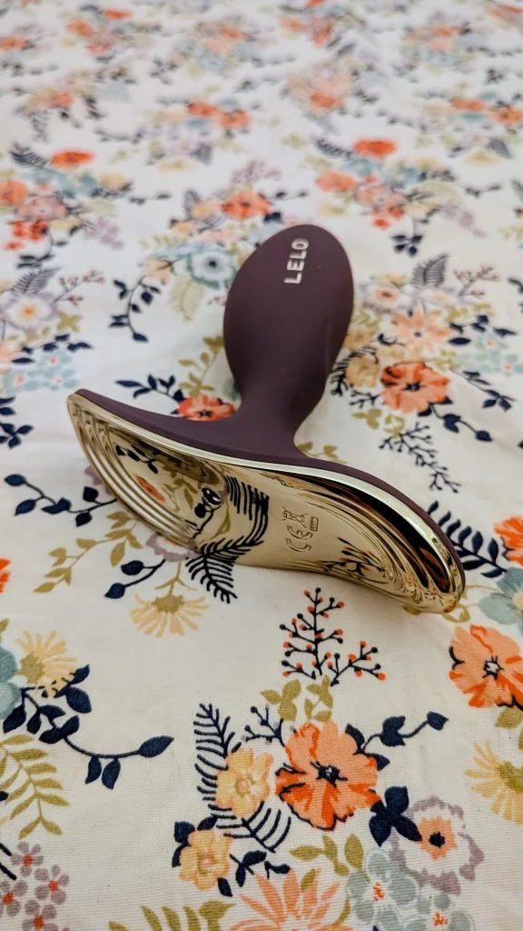 Massajador LELO roxo e dourado sobre tecido floral colorido.