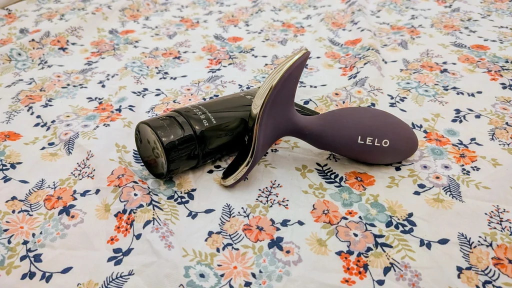Massajador roxo LELO e lubrificante sobre padrão floral.