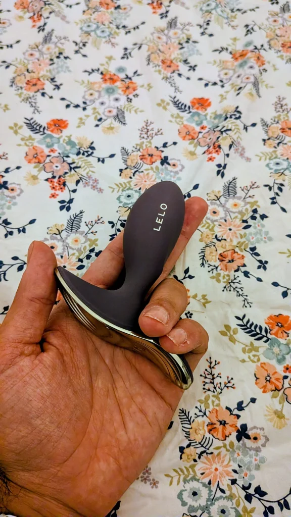 Mão segura massajador LELO sobre fundo floral.