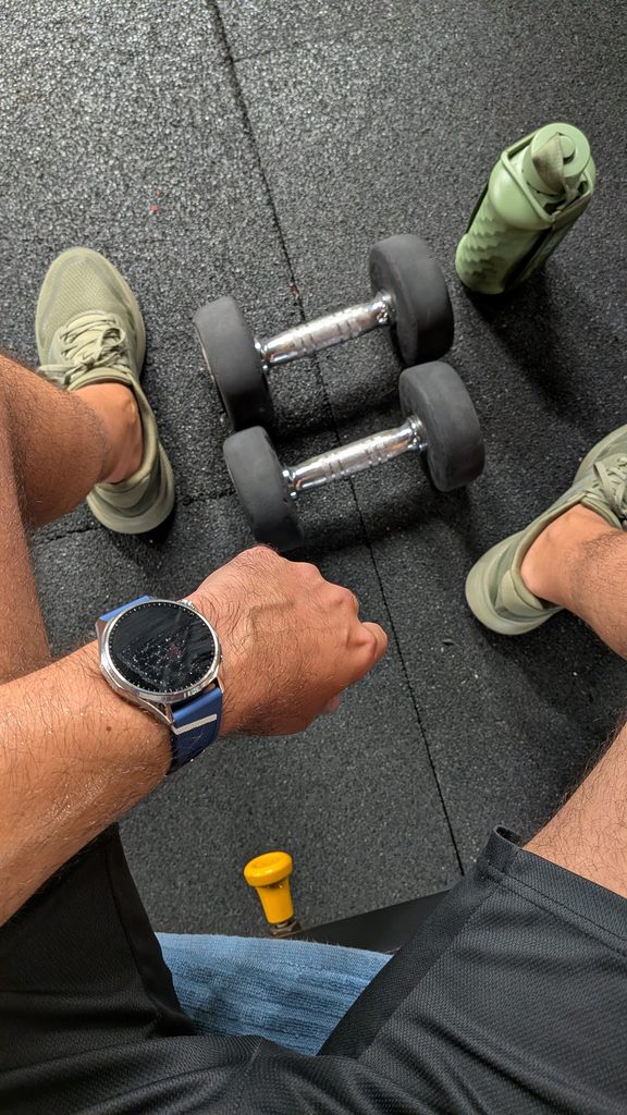 Pessoa no ginásio com halteres, garrafa e smartwatch no pulso.
