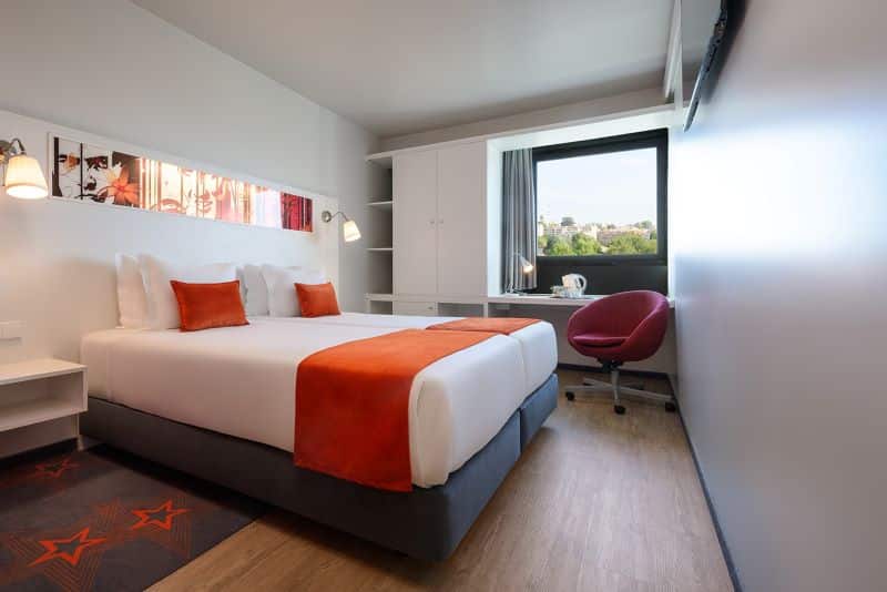 Quarto de hotel moderno com cama e janela grande.