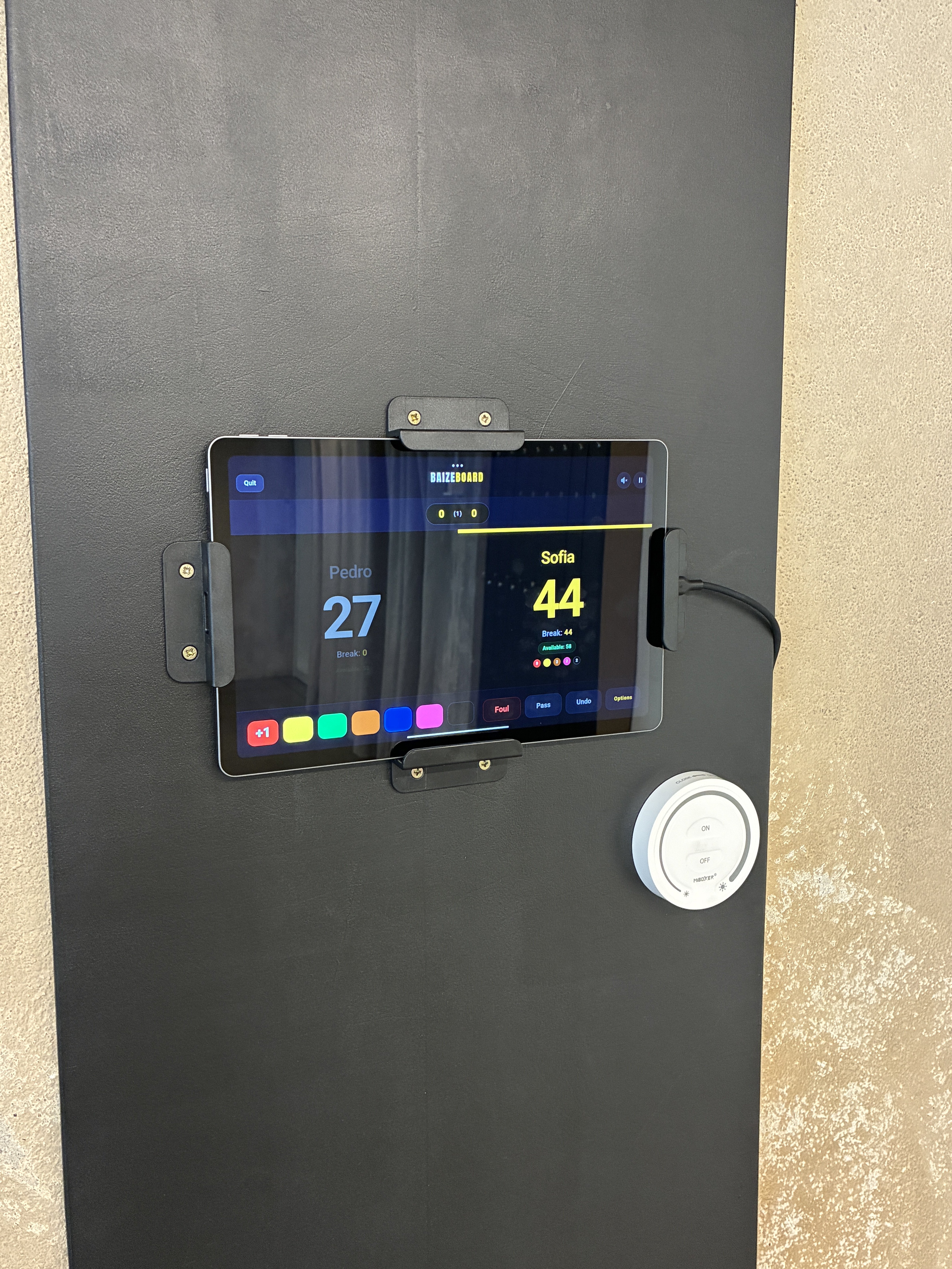 Tablet fixado num painel escuro a exibir a aplicação Baizeboard para registo de pontuação digital num clube de snooker.