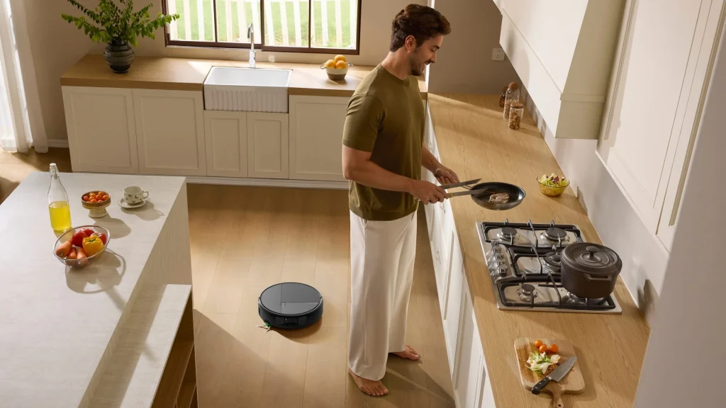 Homem a cozinhar numa cozinha moderna enquanto o aspirador robô Roomba Max 875 Combo limpa o chão de madeira