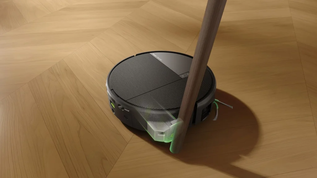 Aspirador robô Roomba Max 875 Combo a limpar um chão de madeira em redor da perna de um móvel com destaque verde na escova lateral