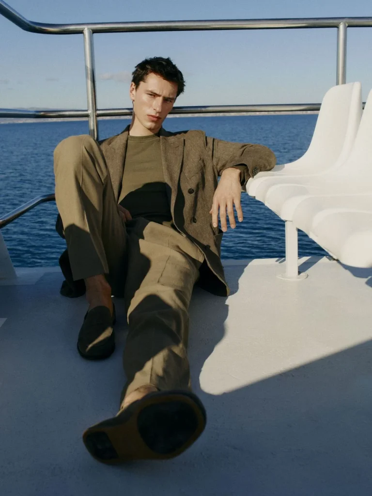 Homem elegante sentado num barco, a olhar para a câmara.