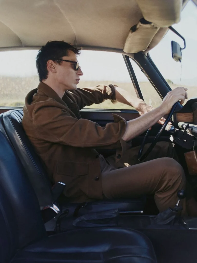 Homem de óculos de sol a conduzir carro clássico.