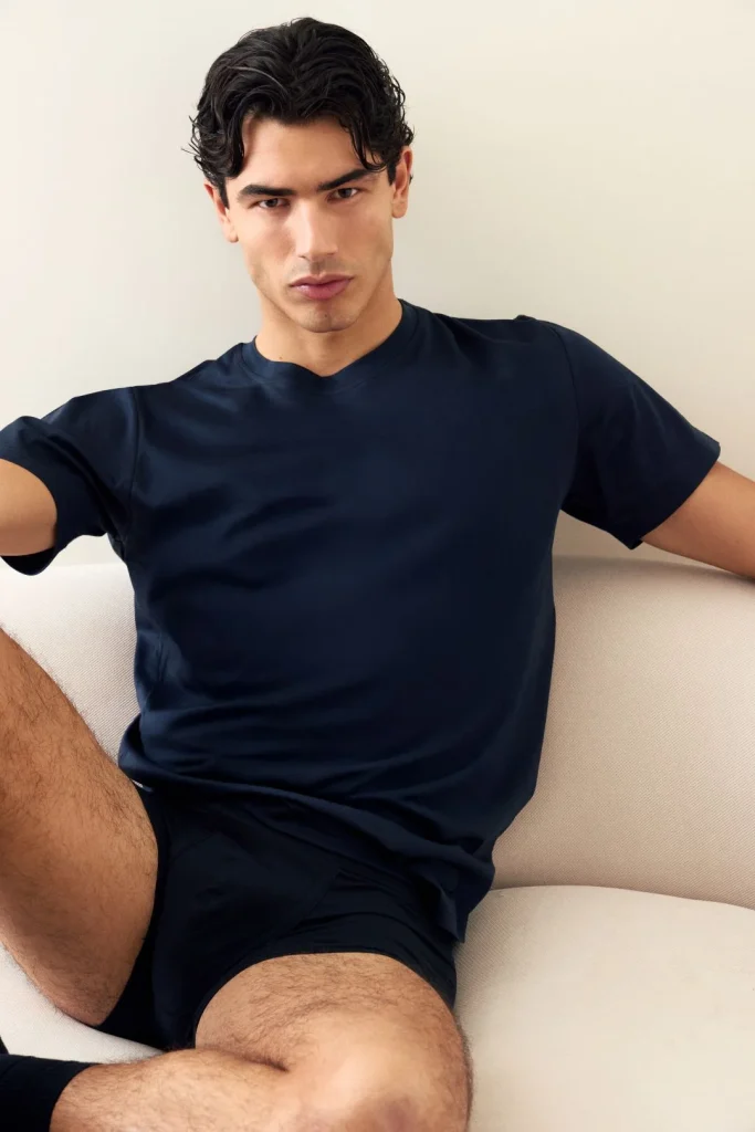 Jovem masculino de t-shirt e boxers azuis sentado no sofá.