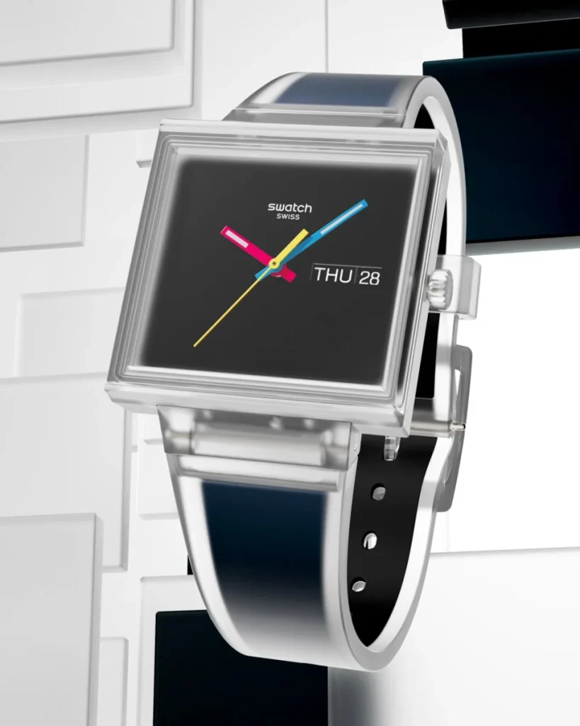 Relógio Swatch quadrado transparente com ponteiros coloridos em fundo branco.