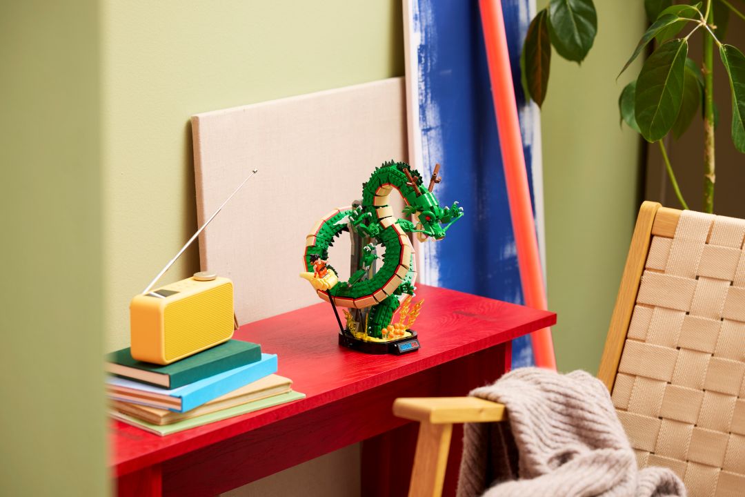 Set LEGO dragão Shenron verde com a minifigura do Songoku exposto numa mesa vermelha ao lado de um rádio amarelo
