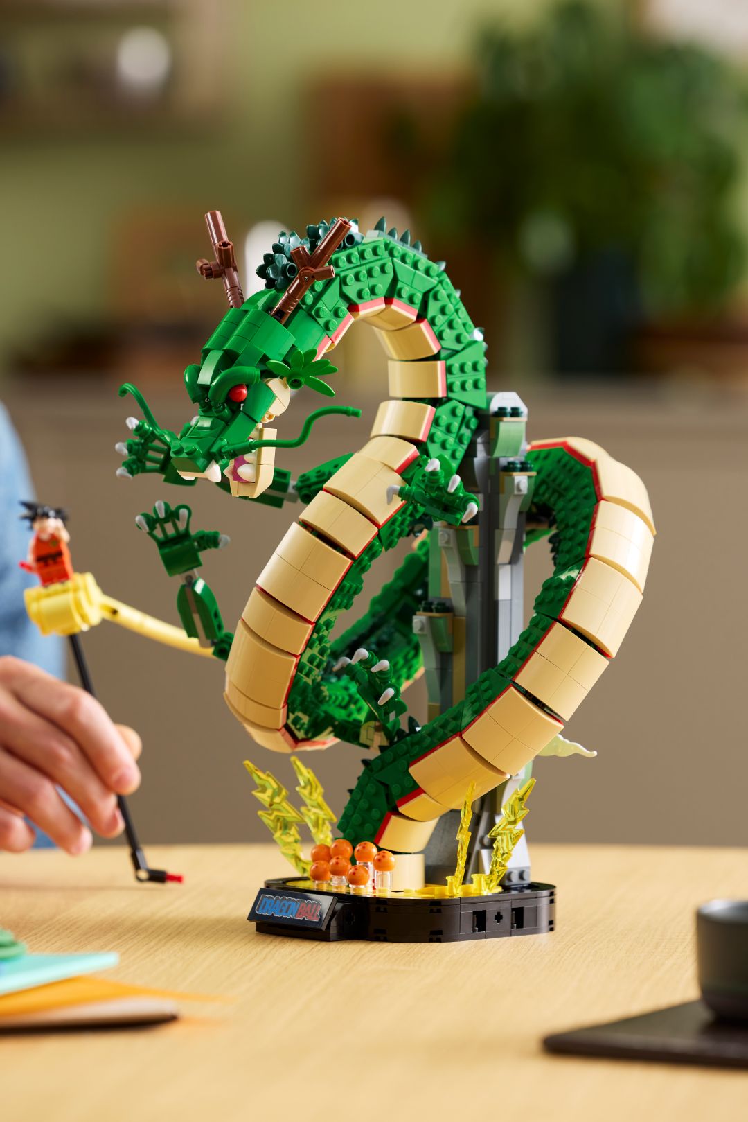 Set LEGO Dragon Ball com o dragão verde Shenron sobre uma base preta com as bolas de cristal e uma mão a posicionar a minifigura do Songoku na nuvem mágica amarela.