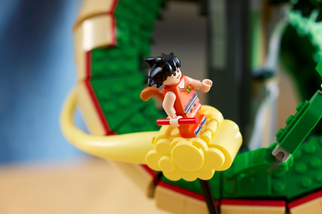 Minifigura do Songoku com fato laranja e bastão na Nuvem Mágica amarela do set LEGO com o corpo verde do dragão Shenron no fundo