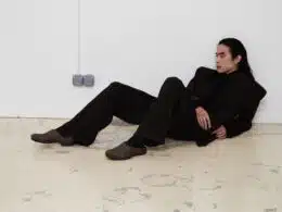 Pessoa sentada no chão com fato preto.