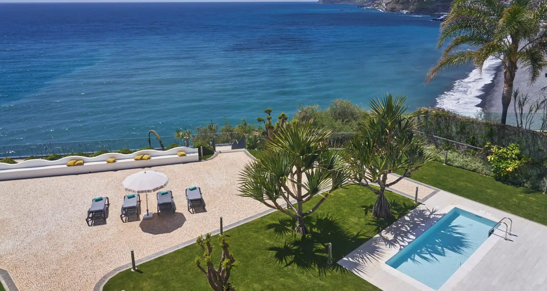 Vista de jardim com piscina e mar ao fundo.