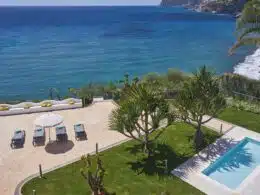 Vista de jardim com piscina e mar ao fundo.