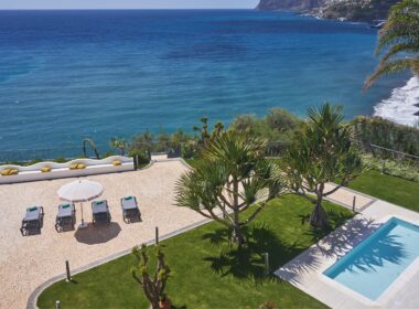 Vista de jardim com piscina e mar ao fundo.