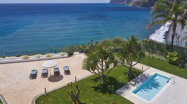 Vista de jardim com piscina e mar ao fundo.