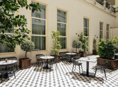 Pátio exterior com mesas e cadeiras, arborizado.