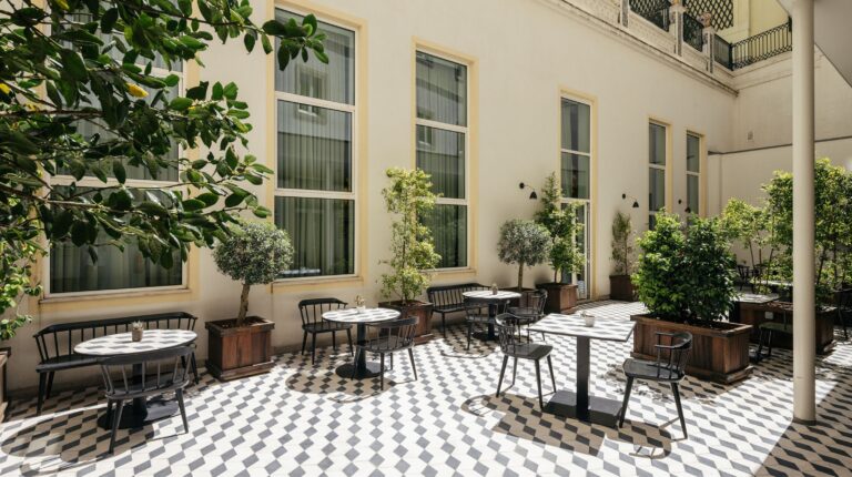 Pátio exterior com mesas e cadeiras, arborizado.