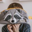 Criança segura estojo cinza com desenho de guaxinim
