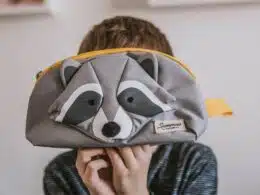 Criança segura estojo cinza com desenho de guaxinim