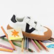 Sapatilha infantil sobre lápis de cor e desenhos.