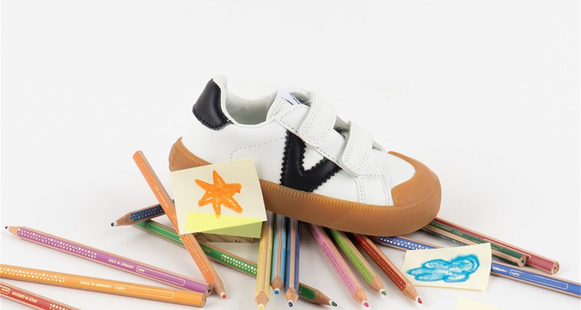 Sapatilha infantil sobre lápis de cor e desenhos.