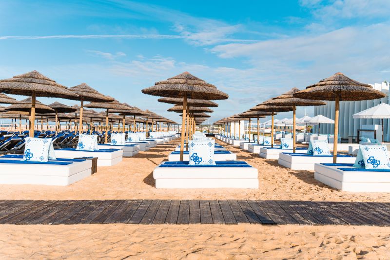Praia com espreguiçadeiras e chapéus de palha alinhados.
